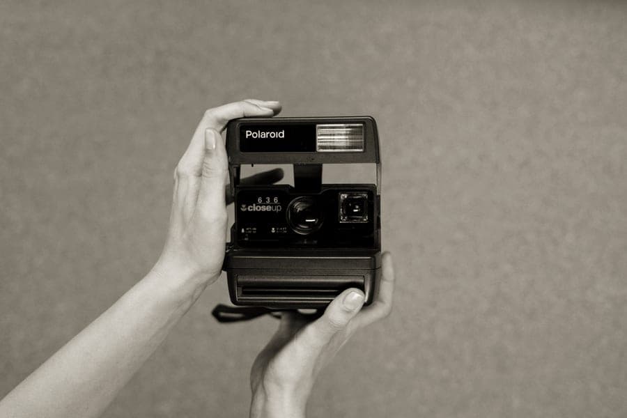 Hands holding a small instant camera, framing a shot